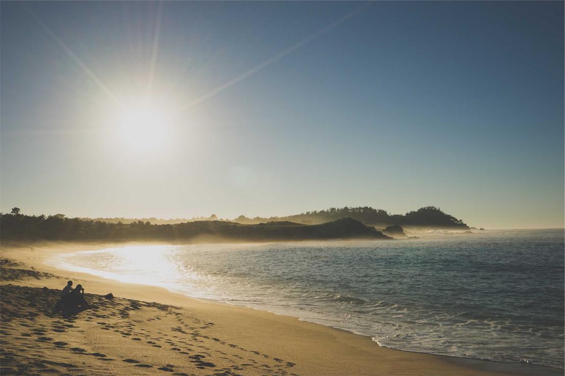 A serene beach scene with footprints in the sand. The sun shines brightly over the calm ocean waters.