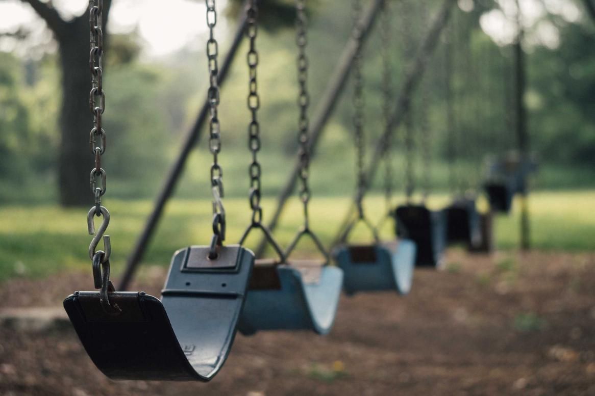 A row of empty swings in a park. The swings are hanging from chains.