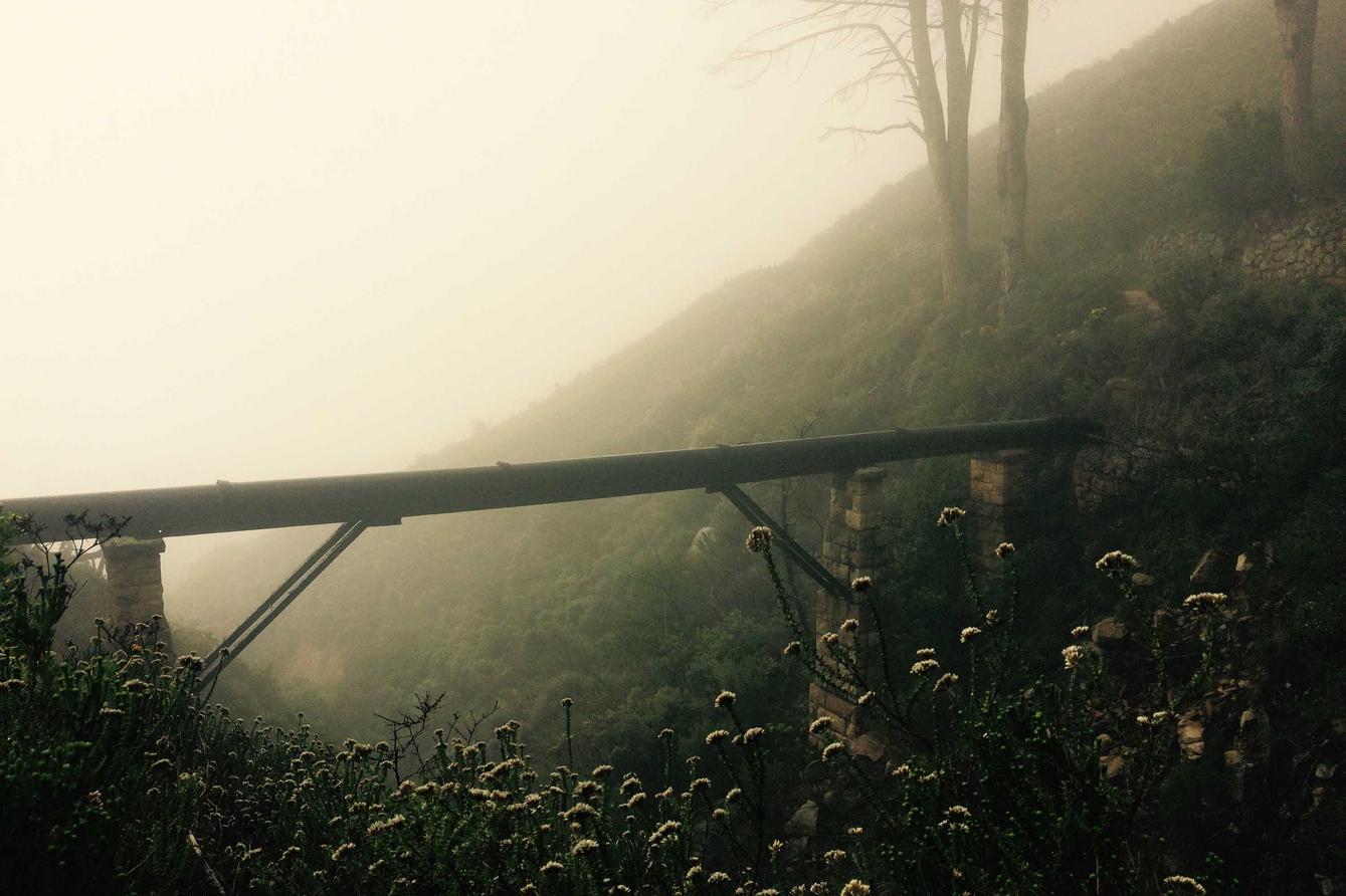 A bridge on a hillside shrouded in fog. The bridge has a metal frame.
