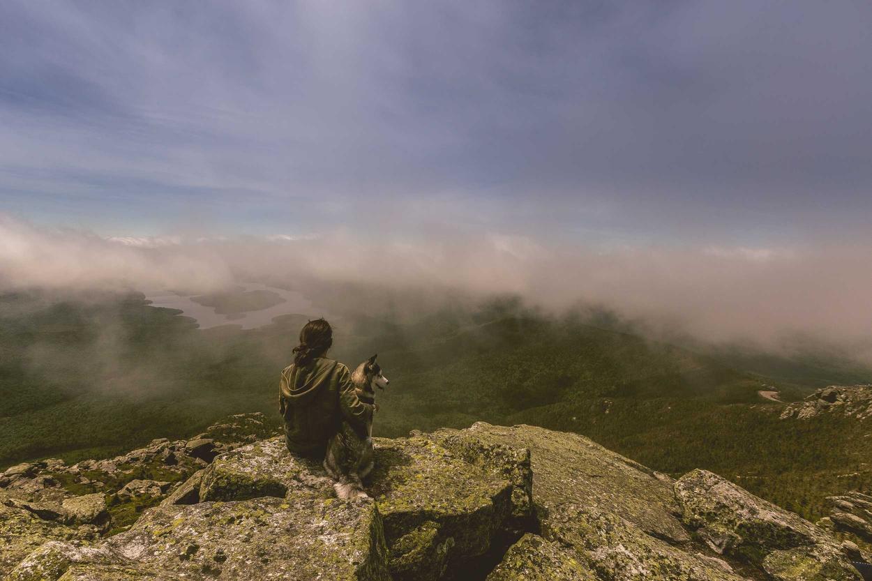 Man sitting on mountain peak. He is overlooking a foggy valley.