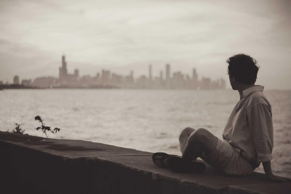 Man sitting on ledge. City skyline in background.