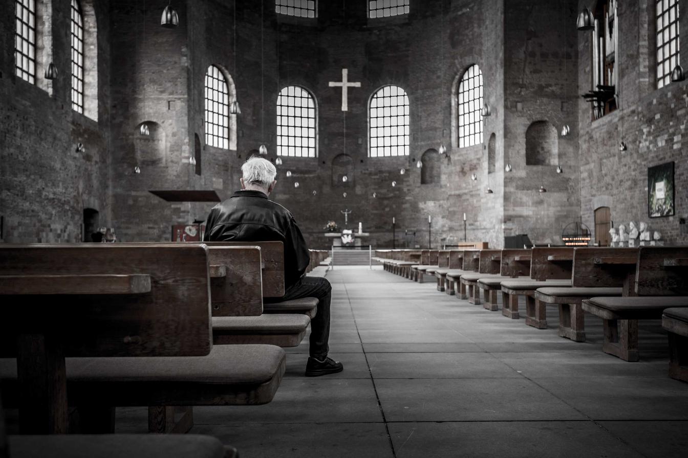 Man sitting alone in a church. He appears to be in deep thought.