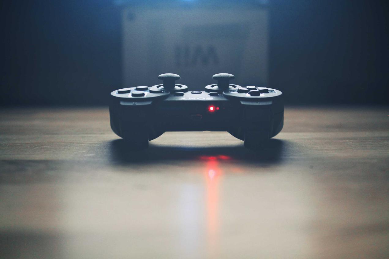 A PS3 controller with a red light on a wooden table. The controller is out of focus.