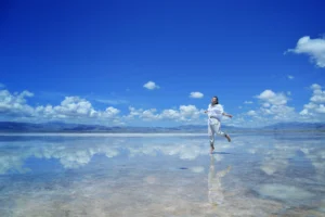 Woman in white running on a reflective surface. The reflection of clouds is visible on the ground.